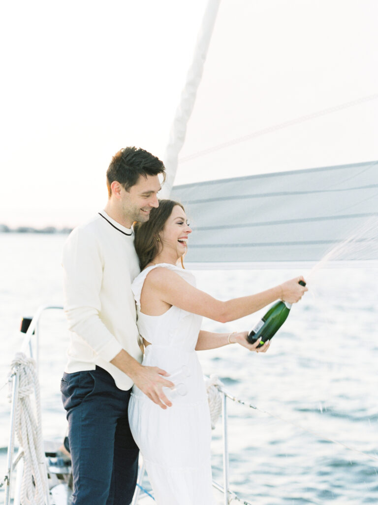Couple pops champagne during sailboat photos