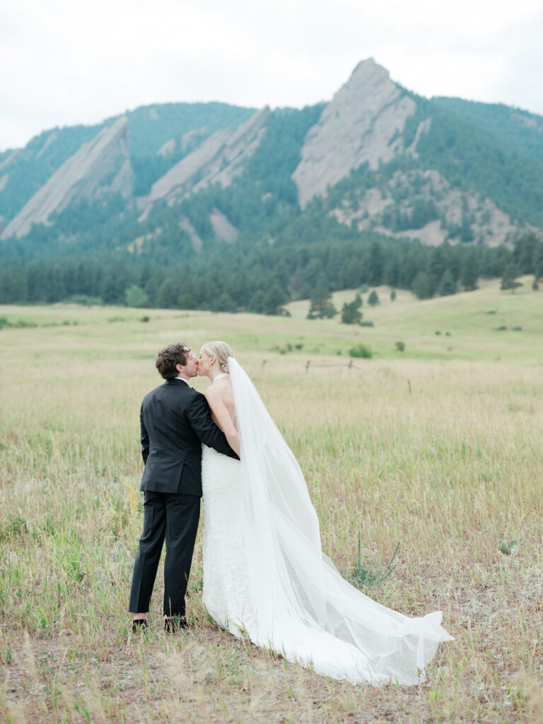 Newlyweds posing with a panoramic Flatiron mountain view during golden hour in Boulder, Colorado.